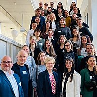 Teilnehmende des Netzwerktreffens Nachhaltigkeit und Gesundheit stehen gemeinsam auf einer Treppe, die zum Audimax der ASH Berlin führt.
