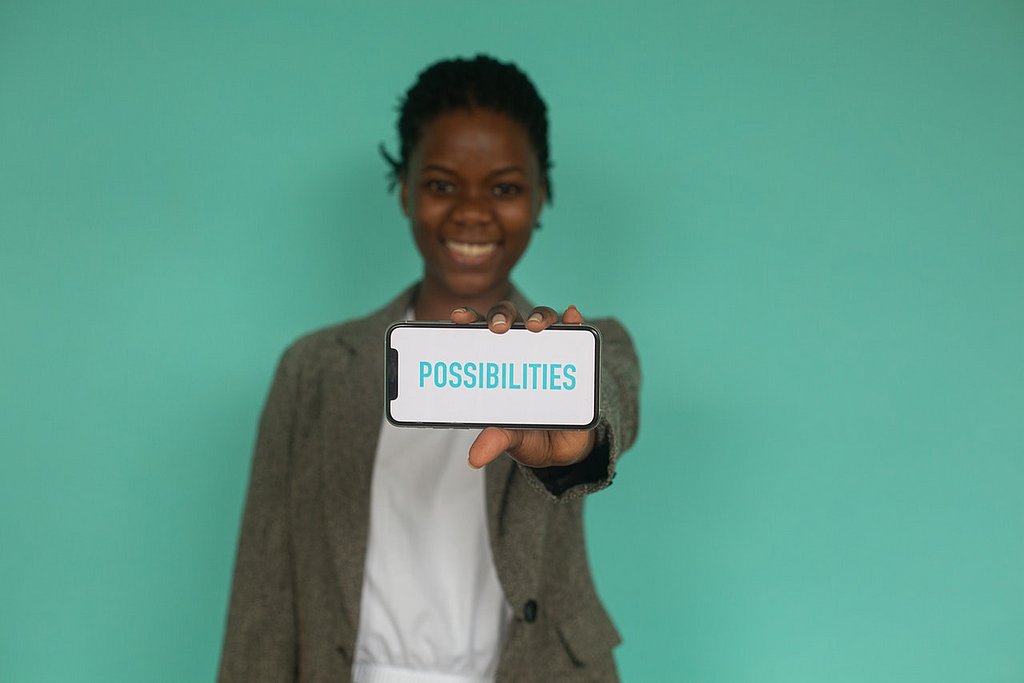 Eine People of Color Frau hält ein Handy vor sich auf dessen Bildschirm "Possibilities" steht